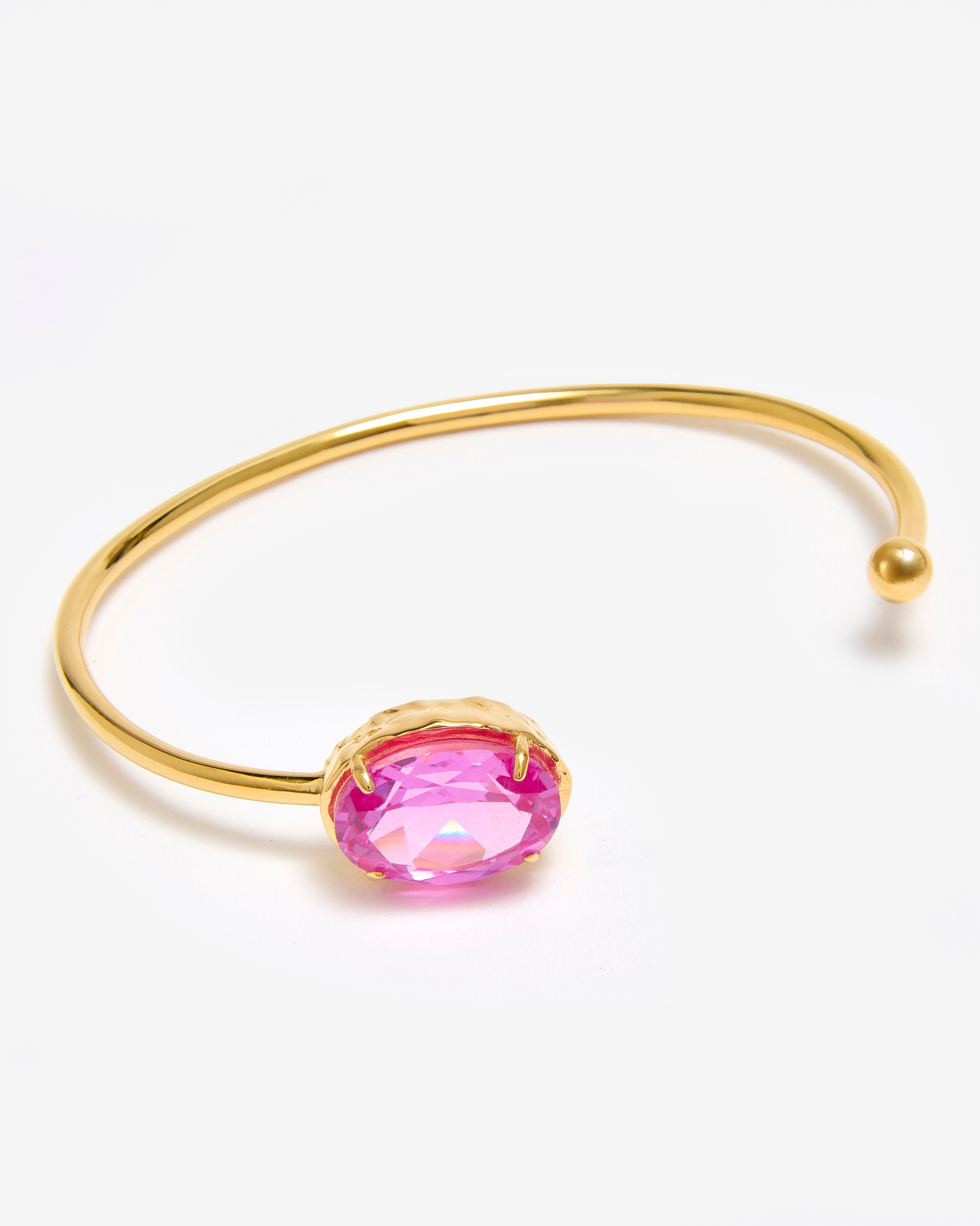 A gold vermeil bracelet by Azora featuring an open cuff design with a single lab grown tourmaline stone in the centre.